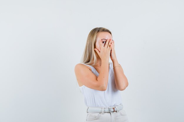 Jeune femme regardant à travers les doigts en chemisier blanc et à l'excitation