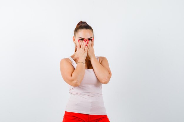 Jeune femme regardant à travers les doigts en débardeur beige et à la peur