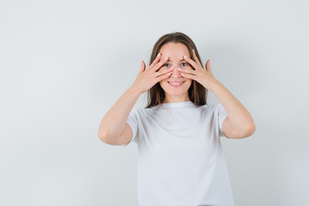 Jeune femme regardant à travers les doigts en t-shirt blanc et à la jolie