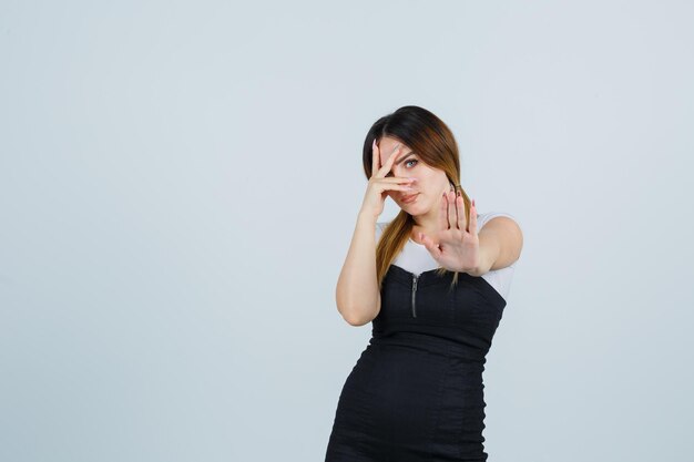 Jeune femme regardant à travers les doigts tout en montrant le geste d'arrêt