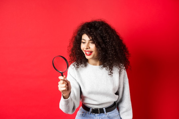 Jeune femme regardant à travers une loupe enquêtant ou recherchant quelque chose de curieux...