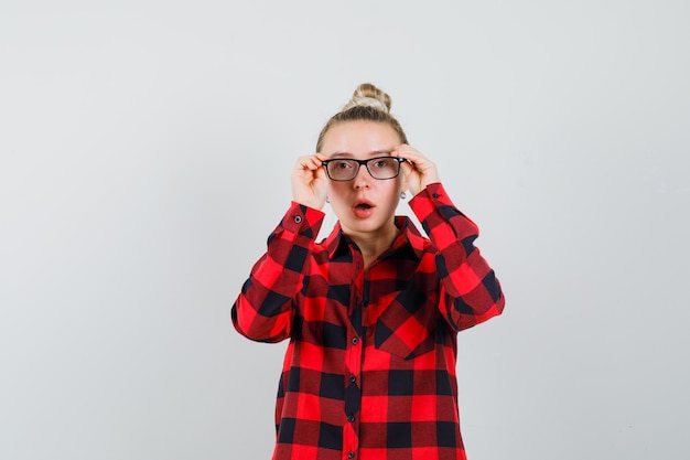 Jeune femme regardant à travers des lunettes en chemise à carreaux et à la surprise