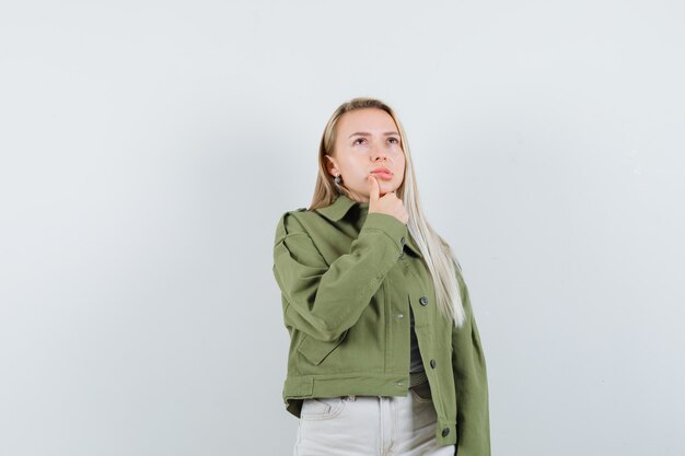 Jeune femme regardant en veste, pantalon et regardant pensif, vue de face.
