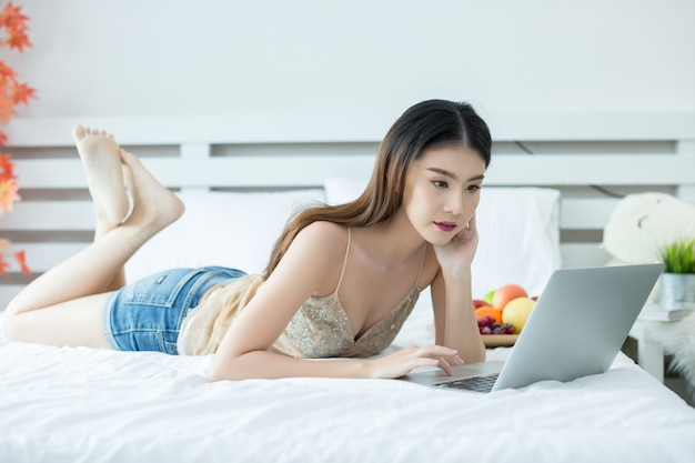 Une jeune femme regarde un film depuis son ordinateur portable sur le lit à la maison