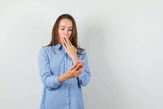 Jeune femme, regarder, téléphone portable, dans, chemise bleue, et, à, choqué