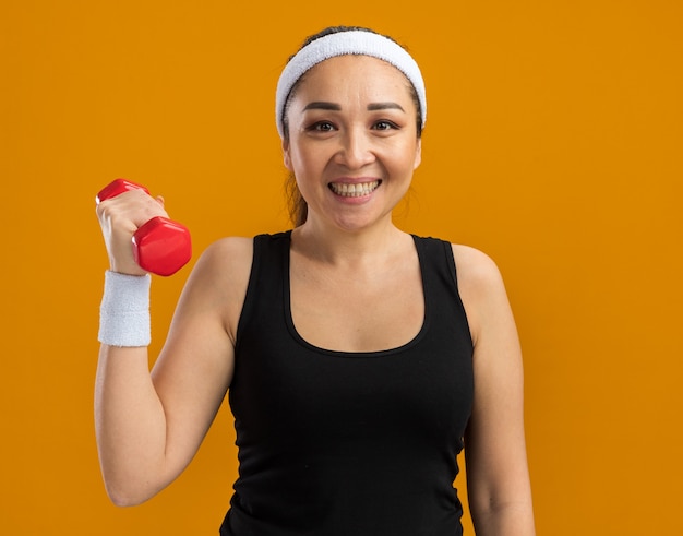 Jeune Femme De Remise En Forme Avec Bandeau Et Brassards Levant Le Bras Avec Haltère Souriant Joyeusement