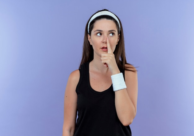 Jeune femme de remise en forme en bandeau à côté en pointant avec le doigt sur son nez debout sur fond bleu