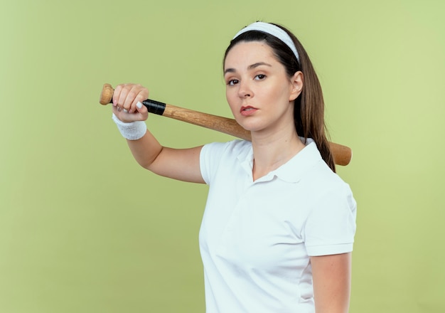 Jeune Femme De Remise En Forme En Bandeau Tenant Une Batte De Baseball Regardant La Caméra Avec Une Expression Confiante Sérieuse Debout Sur Fond Clair