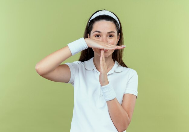 Jeune femme de remise en forme dans le bandeau faisant le geste de temps avec les mains debout sur un mur léger