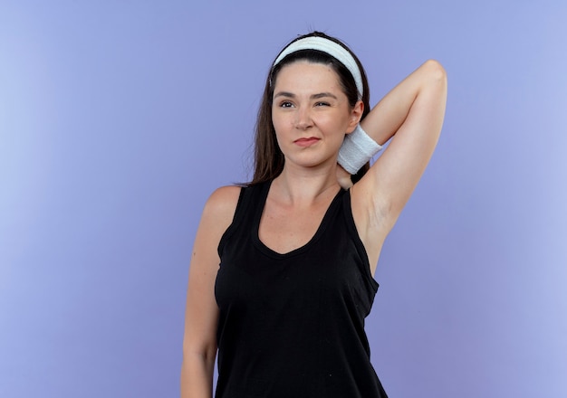 Jeune femme de remise en forme dans le bandeau qui s'étend à la mécontentement debout sur le mur bleu