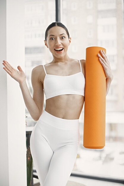 Jeune femme de remise en forme prête pour l'entraînement tenant un tapis de yoga orange