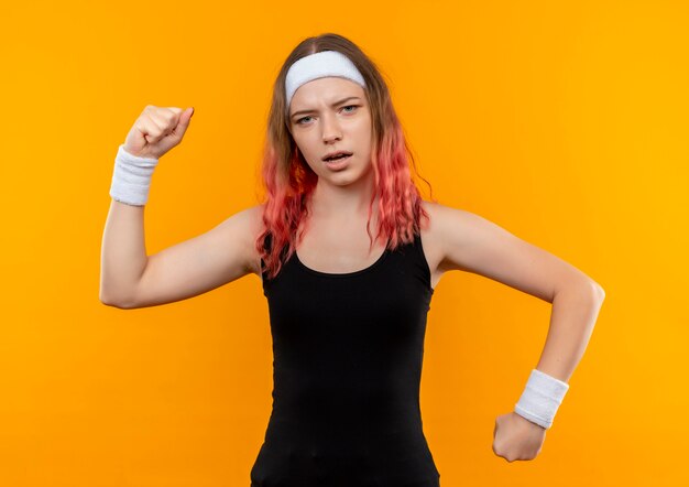 Jeune femme de remise en forme sportswear levant le poing à la confiance debout sur le mur orange