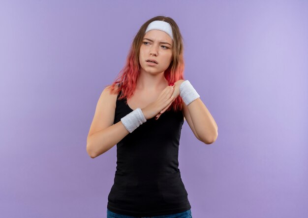 Jeune femme de remise en forme en tenue de sport tenant la main ensemble faisant l'échauffement à côté avec un visage sérieux debout sur un mur violet