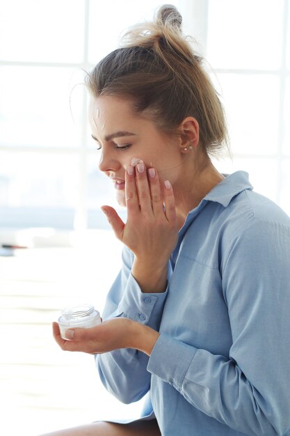 Jeune femme répandant la crème pour le visage. Concept de soins de la peau.