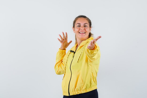 Jeune femme répandant ses paumes ouvertes vers l'avant en imperméable jaune et à la jolly