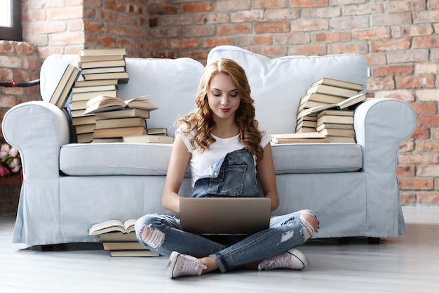 Jeune femme reposant sur le canapé avec ordinateur portable et beaucoup de livres