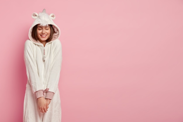 Jeune femme ressent du plaisir, jouit du confort en costume kigurumi doux, tient les mains ensemble