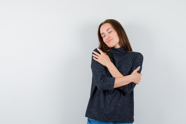 La jeune femme rêve en tenant ses mains sur les épaules sur fond blanc