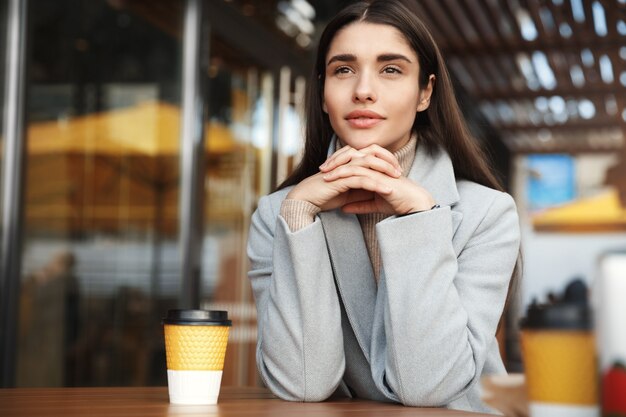 Jeune femme rêveuse, boire du café dans un café et à la recherche dans la rue.