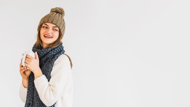 Jeune femme riante en bonnet et écharpe avec une tasse de boisson