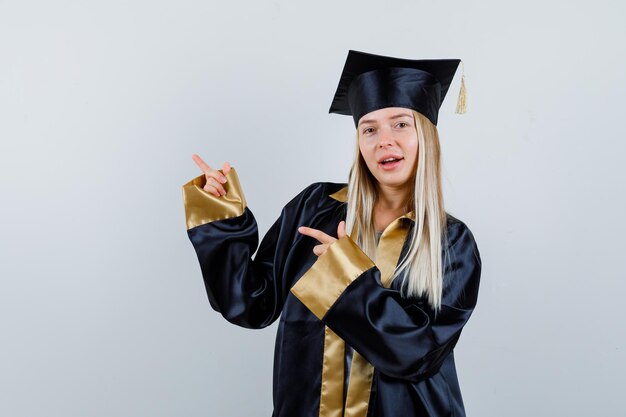 Jeune femme en robe académique pointant de côté et semblant joyeuse