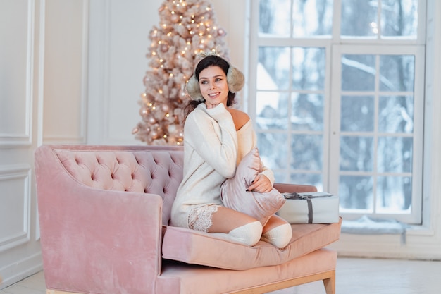 Jeune femme en robe blanche sur le canapé à Noël