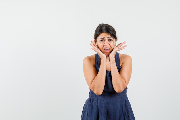 Jeune femme en robe bleu foncé touchant le visage avec les mains et ayant l'air troublé