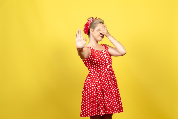 Jeune femme en robe à pois rouge couvrant son visage sur jaune