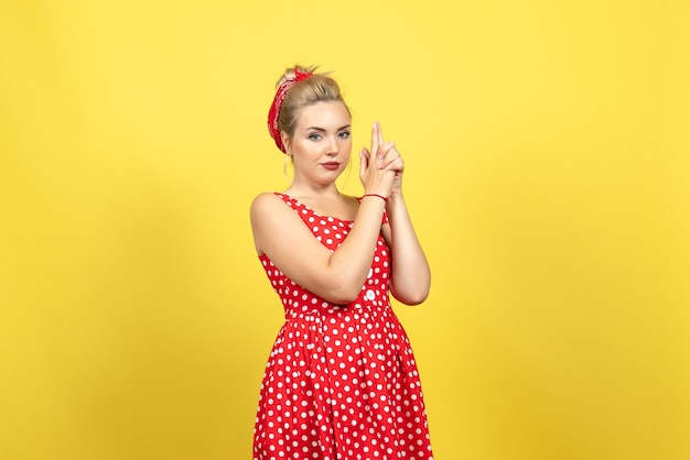 Photo gratuite jeune femme en robe à pois rouge et pistolet tenant pose sur jaune