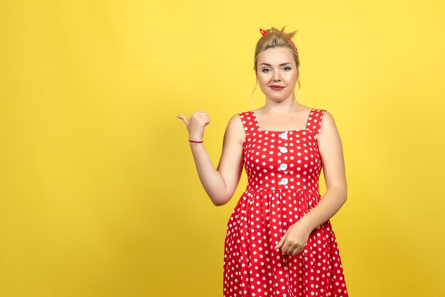 Jeune femme en robe à pois rouge pointant de côté sur jaune