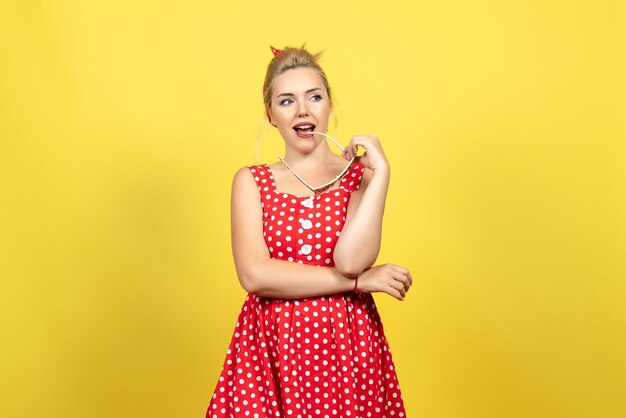 Jeune femme en robe à pois rouge posant avec des lunettes de soleil sur jaune