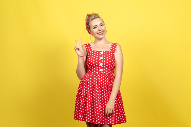 jeune femme en robe à pois rouge posant avec sourire sur jaune