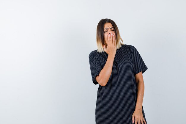 Jeune femme en robe polo bâillements et à la vue de face, somnolent.