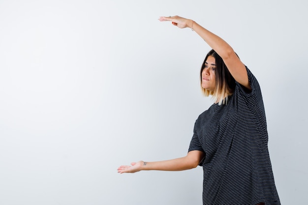 Photo gratuite jeune femme en robe polo montrant le signe de la taille et à la confiance, vue de face.