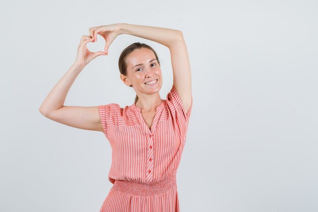 Jeune femme en robe rayée en forme de coeur avec les mains et à la joyeuse vue de face.