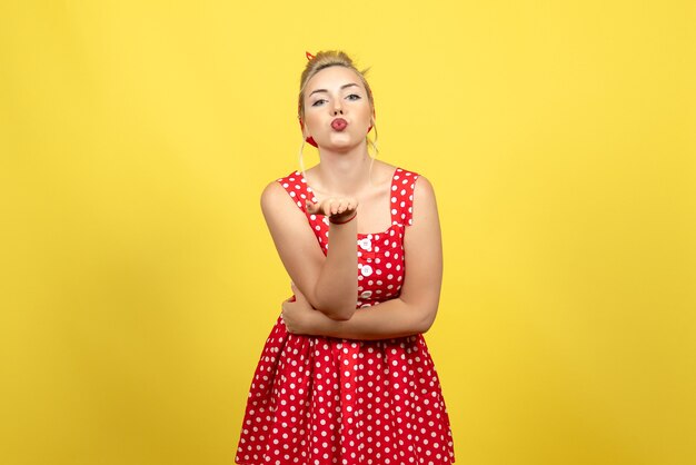 Jeune femme en robe rouge à pois envoyant des baisers aériens sur jaune