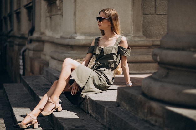 Jeune femme en robe verte assise sur les marches d'un immeuble ancien