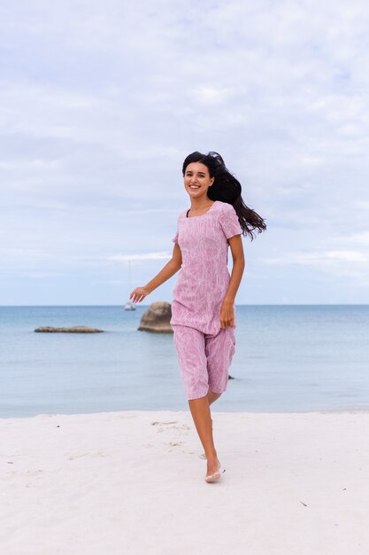Jeune femme romantique aux longs cheveux noirs dans une robe sur la plage en souriant et en riant s'amuser seul