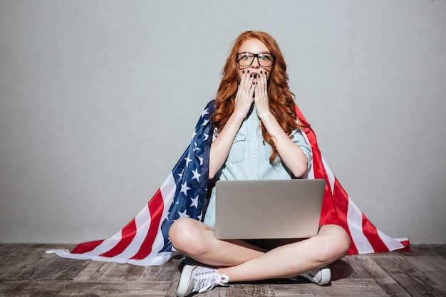 Jeune femme rousse avec le drapeau des États-Unis à l'aide d'un ordinateur portable