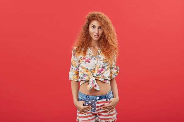 jeune femme rousse avec une longue coiffure frisée qui pose en studio