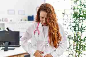 Photo gratuite jeune femme rousse portant un uniforme de médecin et un stéthoscope à la clinique avec la main sur le ventre parce que l'indigestion maladie douloureuse se sentant mal mal concept