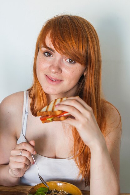 Jeune femme rousse souriante tenant un sandwich à la main