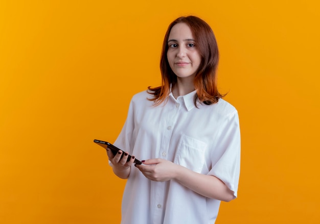 jeune femme rousse tenant téléphone isolé sur jaune