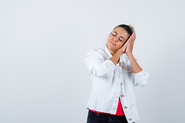 Jeune femme s'appuyant sur les mains comme oreiller en t-shirt, veste blanche et l'air paisible, vue de face.