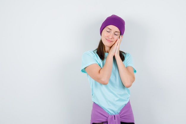 Jeune femme s'appuyant sur les paumes comme oreiller en t-shirt, bonnet et semblant paisible. vue de face.