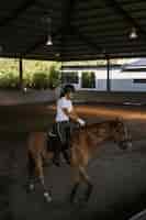 Photo gratuite une jeune femme s'entraîne à l'équitation dans l'arène. jeune femme caucasienne en vêtements formels faisant de l'équitation à travers l'arène sablonneuse. un cheval de race pour le sport équestre. la sportive à cheval
