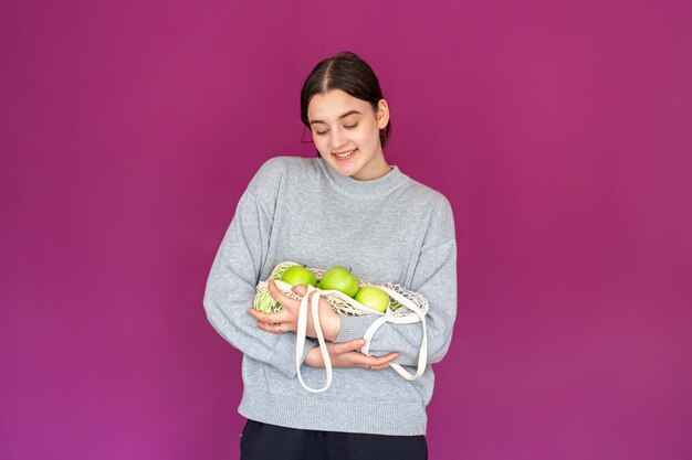 Une jeune femme avec un sac à cordes avec des pommes sur fond rose