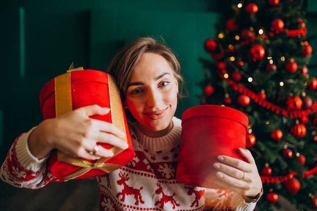 Jeune femme avec sapin de Noël tenant des boîtes rouges