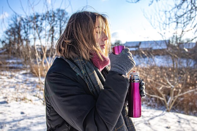 Photo gratuite une jeune femme savoure une boisson chaude dans un thermos lors d'une promenade en hiver