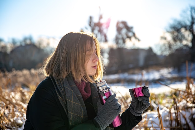 Une jeune femme savoure une boisson chaude dans un thermos lors d'une promenade en hiver